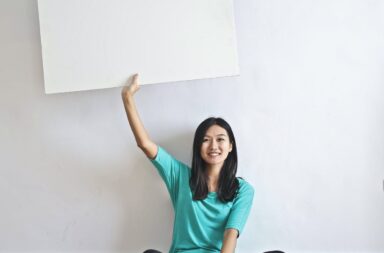 smiling ethnic woman with blank poster in empty flat